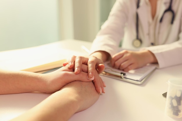 O médico coloca a mão nas mãos do paciente sentado com ela no apoio e empatia da clínica médica