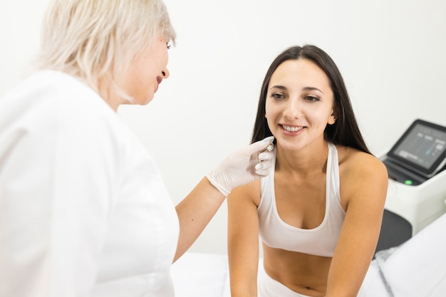 O médico cosmetologista examina a pele do rosto do paciente