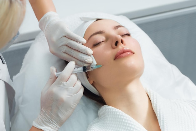 O médico cosmetologista faz o procedimento de injeções faciais rejuvenescedoras para apertar e