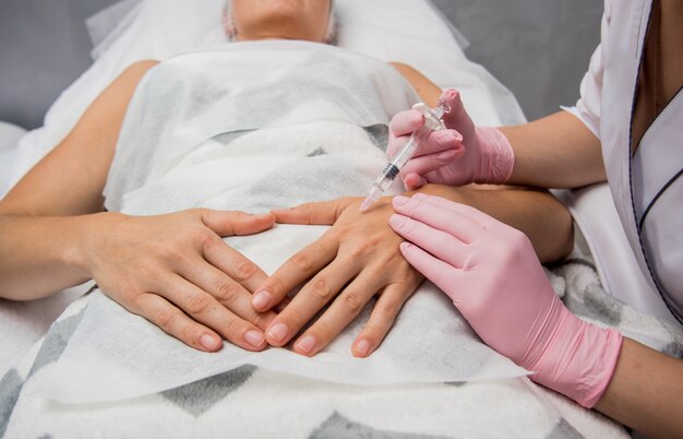 O médico cosmetologista faz o procedimento de injeções nos braços. Jovem mulher em um salão de beleza.