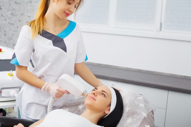 O médico-cosmetologista faz o procedimento Microcorrente terapia da pele facial de uma mulher jovem e bonita em um salão de beleza.Cosmetologia e cuidados com a pele profissional.