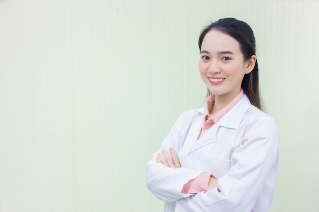 O médico da mulher asiática está cruzando o braço e sorrindo enquanto ela veste o jaleco branco.