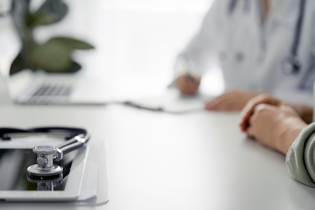 O médico e o paciente estão sentados e discutindo algo na mesa no escritório da clínica o foco é no estetoscópio deitado na mesa de perto conceito de serviço médico e medicina perfeito
