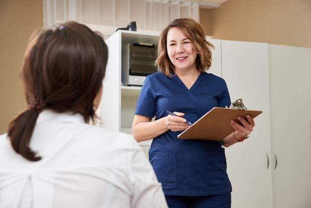 O médico está conversando com uma paciente jovem e fazendo anotações enquanto está em seu consultório