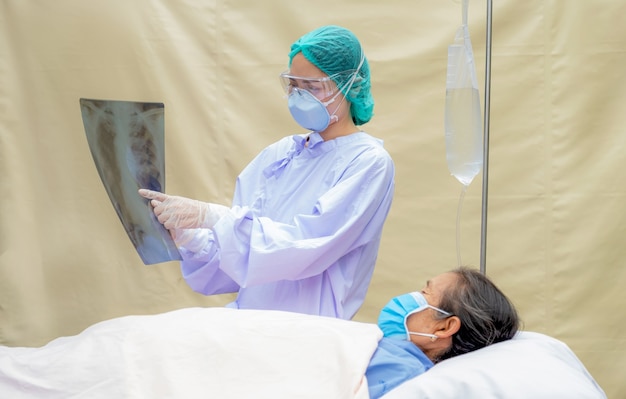 O médico está explicando os resultados da radiografia pulmonar a um paciente idoso que está deitado na cama no quarto do hospital.