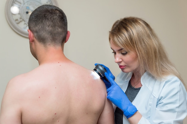 O médico examina a pele do paciente com um dispositivo óptico