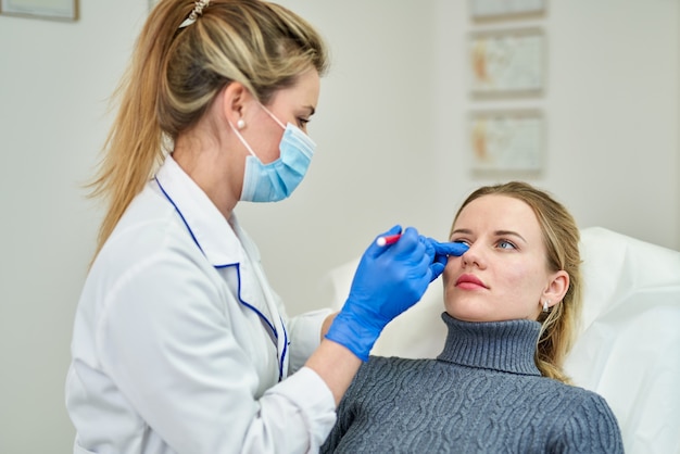 O médico faz uma marcação no rosto de uma bela mulher antes do procedimento do cometa para corrigir o formato do rosto