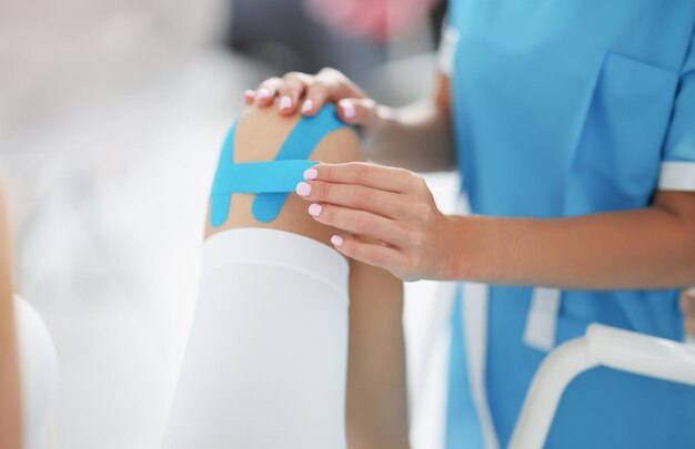 Foto o médico fixa a fita de kinesio na perna do paciente.