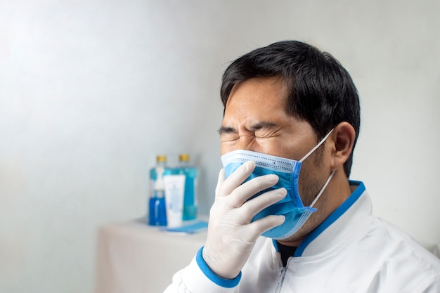 O médico tossindo em uma máscara médica em uma sala branca do hospital.