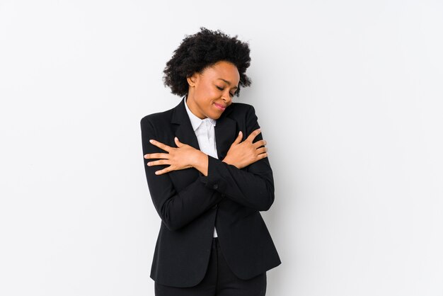 O meio envelheceu a mulher de negócio afro-americano contra uma parede branca abraços isolados, sorrindo despreocupado e feliz.