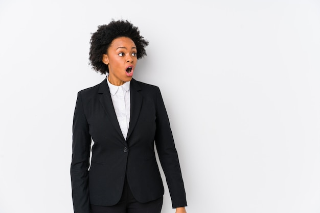 Foto o meio envelheceu a mulher de negócio afro-americano contra uma parede branca isolada sendo chocado por causa de algo que viu.