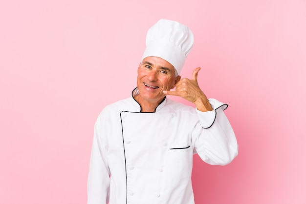 O meio envelheceu o homem do cozinheiro isolado mostrando um gesto de chamada de telefone móvel com dedos.