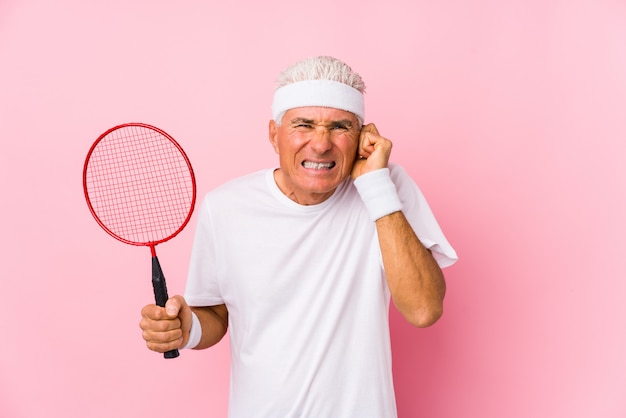 O meio envelheceu o homem que joga o badminton isolado cobrindo as orelhas com as mãos.