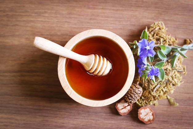 Foto o mel flui de uma concha de mel na mesa de madeira e flor seca em fundo de madeira, mel orgânico