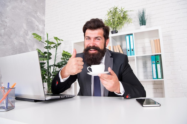 O melhor corretor de imóveis de chá dá os polegares para cima com uma xícara de chá Advogado bebe chá no escritório Homem barbudo aproveita a pausa para o chá no local de trabalho Vida no escritório Trabalho diurno Pausa para descanso no trabalho Manhã e café da manhã