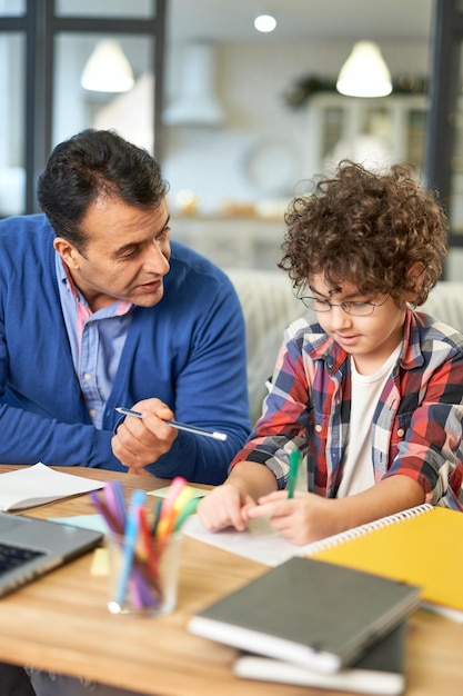 O melhor professor que ama um pai hispânico ajudando seu filho com o dever de casa, explicando a tarefa enquanto está sentado