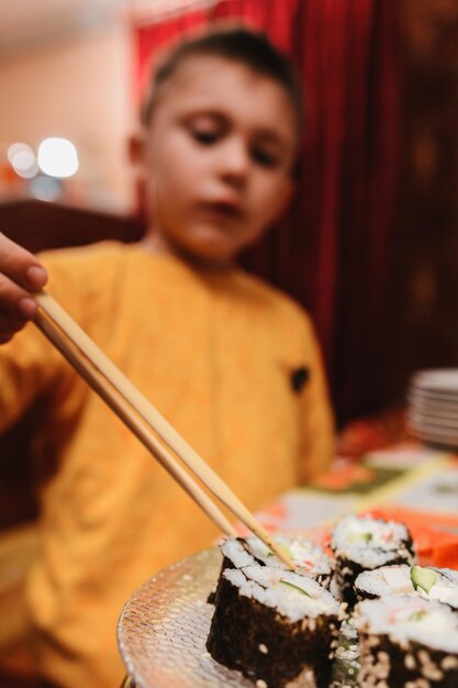 O menino adolescente leva o rolo de sushi do prato para comer