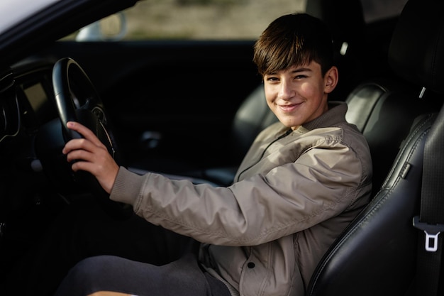 O menino adolescente senta-se no carro do músculo Motorista adolescente novo