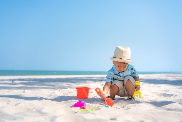 O menino asiático da criança da criança de dois anos que joga com praia brinca na praia.