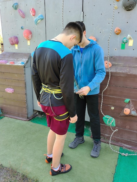 O menino atleta se prepara para escalar a parede de escalada e coloca o equipamento com o treinador