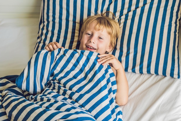 O menino bonito acordou em sua cama. Conceito de sono de crianças.