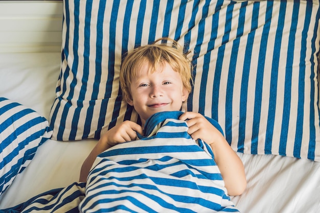 O menino bonito acordou em sua cama. Conceito de sono de crianças.