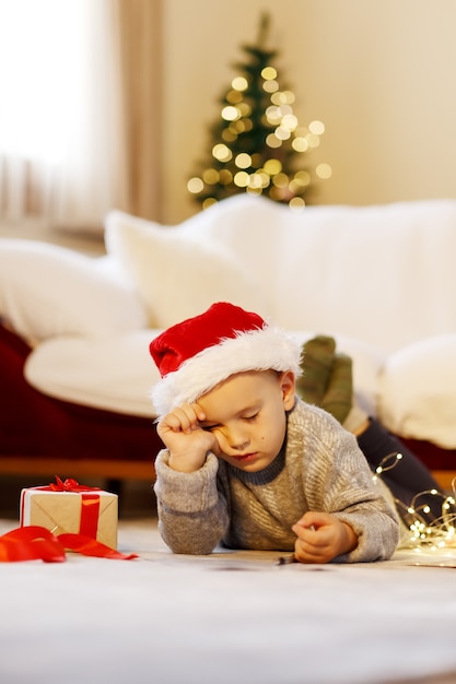 O menino bonito com um boné vermelho adormeceu escrevendo cartas para o Papai Noel. Conceito de Natal.
