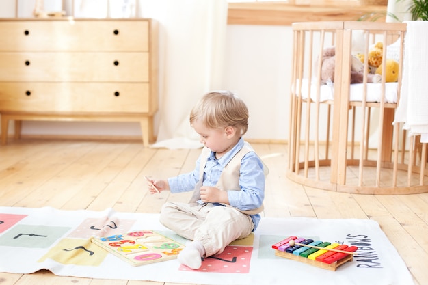 O menino brinca com brinquedos de madeira em casa. brinquedos educativos de madeira para a criança. retrato de um menino sentado no chão no quarto das crianças no estilo escandinavo. brinquedos ecológicos, decoração de quarto de criança