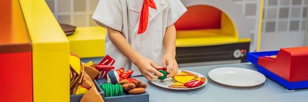 O menino brinca na cozinha de brinquedo cozinha um formato longo de banner de pizza