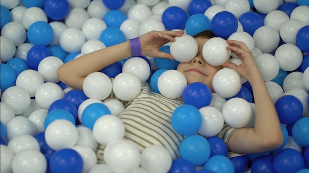 O menino brinca na piscina com bolas de plástico coloridas e as joga