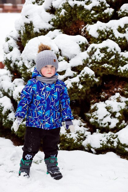 O menino caminha no parque no inverno quando nevou muito esculpindo bonecos de neve