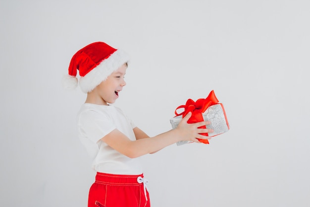 O menino de chapéu de Papai Noel vermelho segurando a caixa de presente