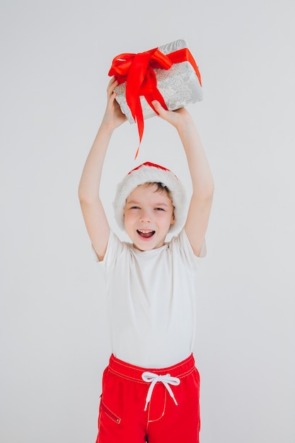 O menino de chapéu de Papai Noel vermelho segurando a caixa de presente