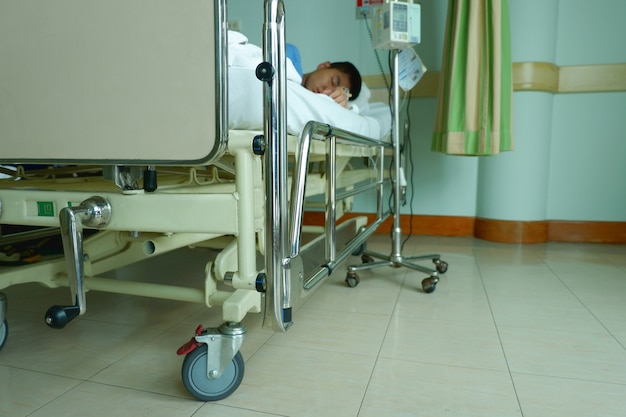 O menino do adolescente estava doente e dorme com o equipamento O tubo IV da bomba da infusão no hospital