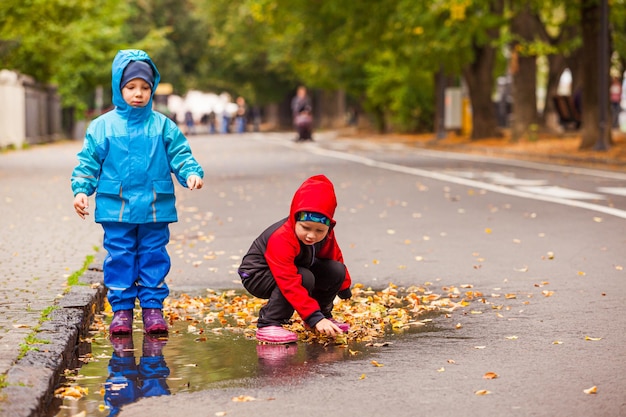 O menino e a menina estão de pé na poça durante a caminhada de outono