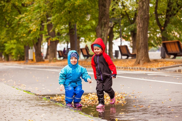 O menino e a menina felizes estão brincando em uma poça andando na rua