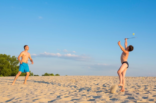 O menino e seu pai estão jogando badminton de praia e desfrutando de bom humor na praia de verão