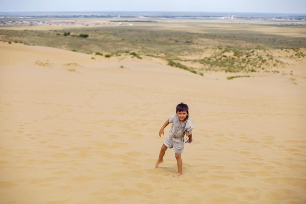 O menino é uma criança que viaja com um terno de rastreador de arqueólogo e um chapéu sentado na areia do deserto