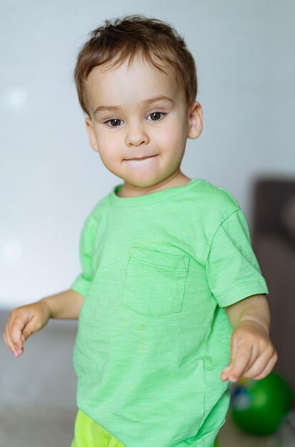 Foto o menino está de pé com uma camiseta verde e sorrindo.