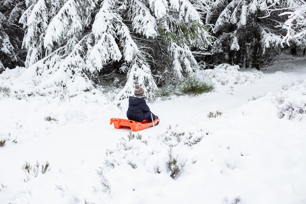 O menino está de trenó em roupas quentes através da floresta de inverno crianças descansam em férias