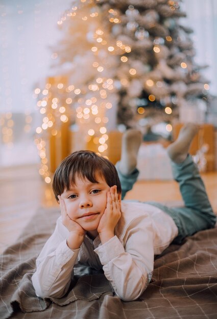 O menino está deitado sob o estilo de vida da árvore de ano novo. Ano Novo e Natal.