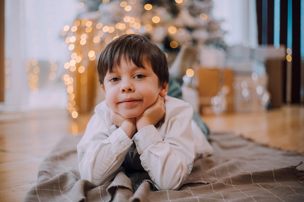 O menino está deitado sob o estilo de vida da árvore de ano novo. Ano Novo e Natal.