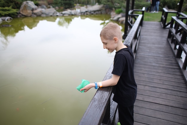 O menino está em uma ponte de madeira no lago e alimenta peixes koi japoneses