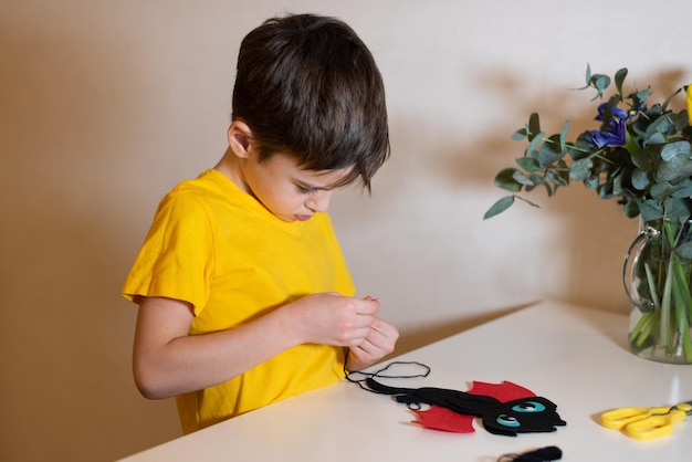 o menino está fazendo bordado Costurando um brinquedo macio de mãos de feltro closeup Passatempo em casa