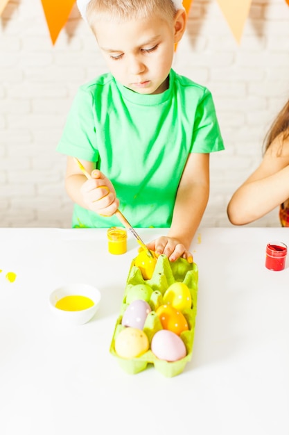 O menino está pintando ovos de Páscoa coloridos na mesa. O menino se prepara para a Páscoa