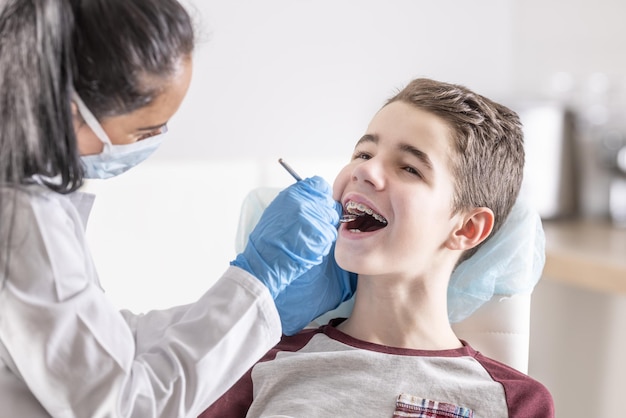 O menino está sentado no dentista verificando o aparelho dentário