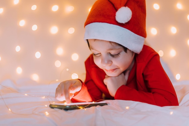 O menino está sentado no telefone no fundo de um clima festivo de ano novo e Natal