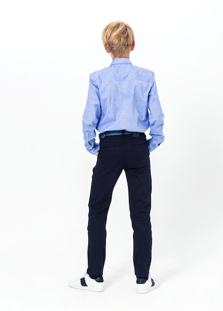 O menino está vestindo uma calça de camisa azul e tênis Um menino demonstra um uniforme escolar por trás da parte de trás Foto vertical
