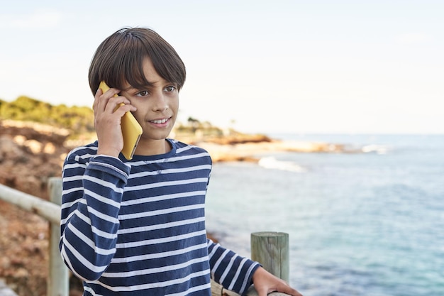 O menino falando no celular à beira-mar