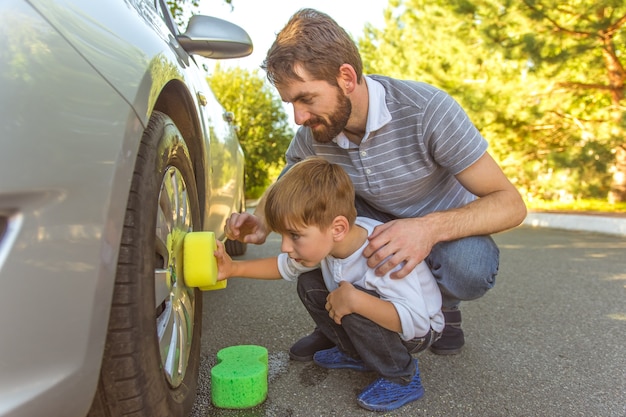 O menino feliz e um pai limpam a roda de um carro